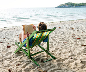 Werbe-Lesezeichen bedrucken Sie bei laprinta Eine Frau im Liegestuhl liest am Strand in der Sonne ein Buch