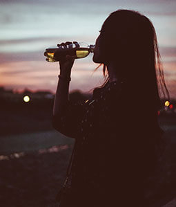 Werbe-Trinkflasche bedrucken Sie bei laprinta Eine Frau trinkt aus einer Trinkflasche in der Abenddämmerung
