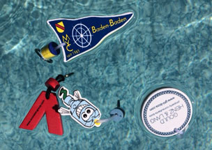 Verschiedene schwimmfähige Schlüsselanhänger in Wunschform mit Kunden-Werbedruck, die in einem Pool schwimmen