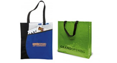 Eine blaue Einkaufstasche aus NonWoven mit lanbgen, schwarzen Henkeln und einem schwarzen eingewebtren Wellen-Higlight an der Seite. Der Werbedruck in Orange ist gut sichtbar. Daneben steht eine laminierte Tasche im Querformat mit kurzen Henkeln, der Logodruck wurde schwarz umgesetzt.